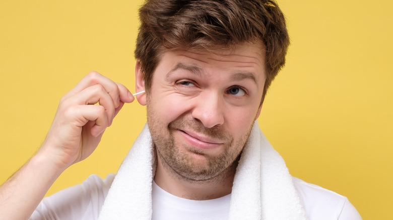 man using cotton swab to clean earwax