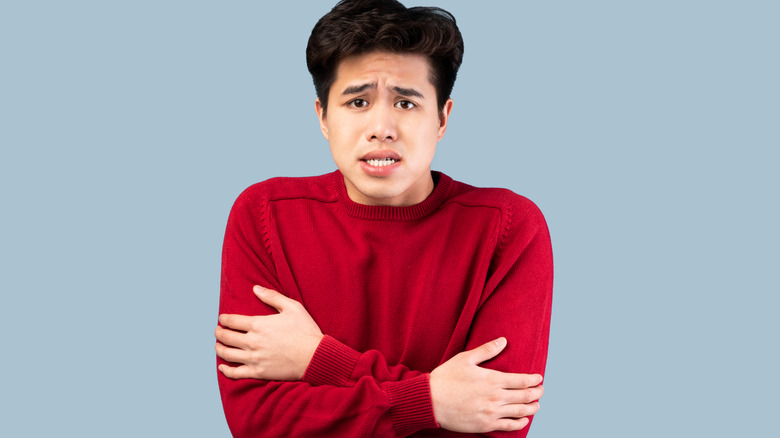 Man shivering and wearing a red sweater, standing against a gray background