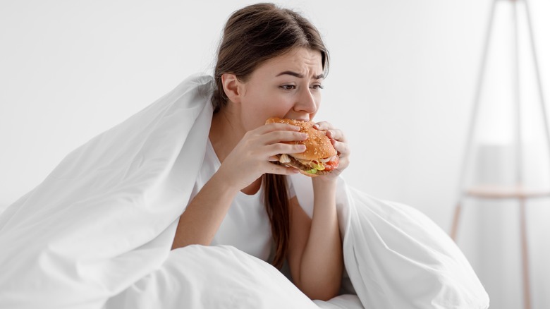sad woman eating burger in bed