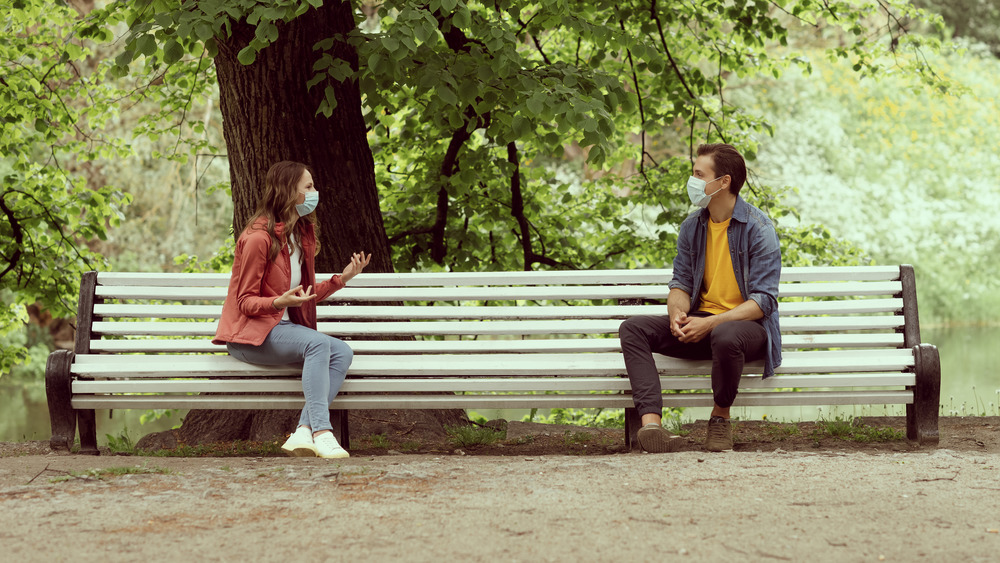 Masked couple talking on park bench