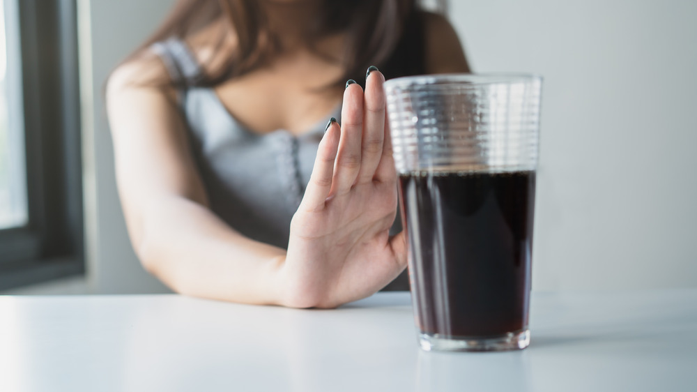 Young woman pushing away a glass of soda 