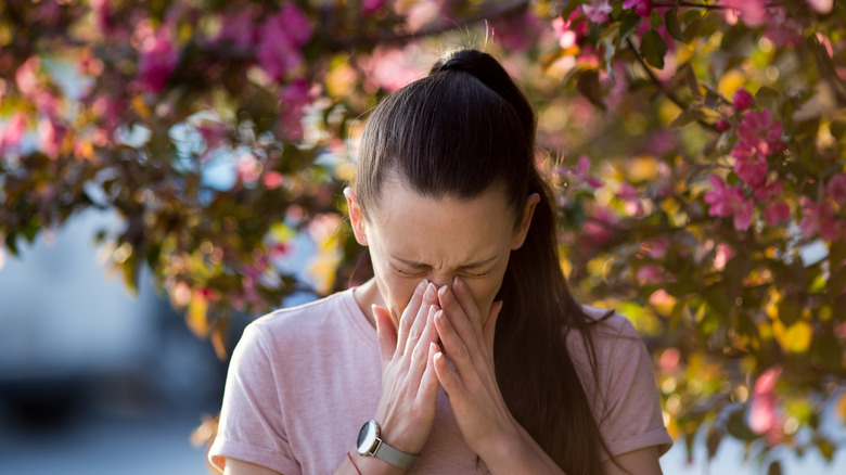 Woman sneezing in front of budding flowers