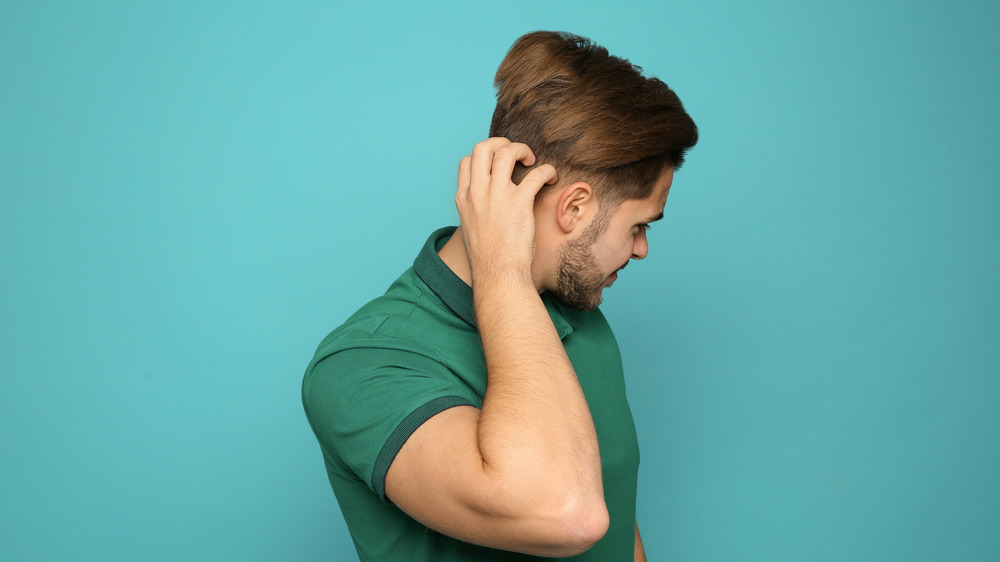 A male itching his scalp with an all green background 