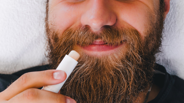 Bearded man holding a stick of lip balm up to his mouth