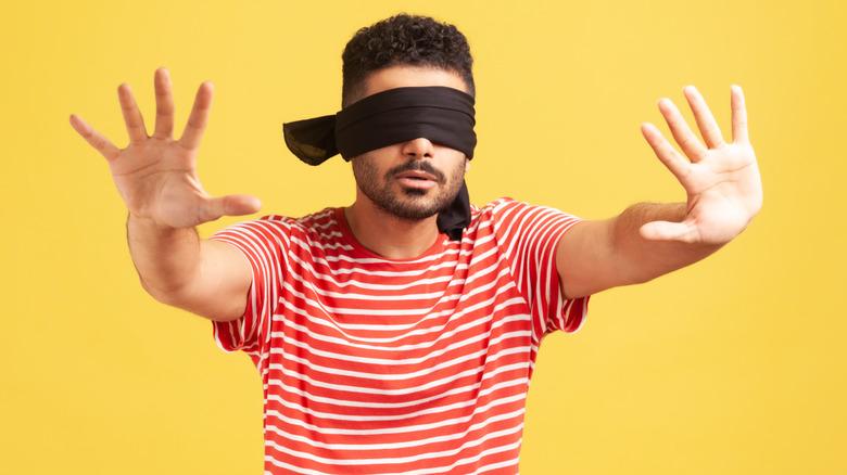 Confused bearded man in red striped t-shirt with blindfold on eyes with outstretched arms