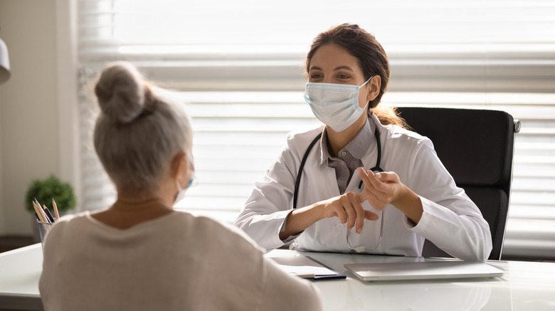 ﻿﻿Female doctor in medical facial mask having consultation with elderly patient