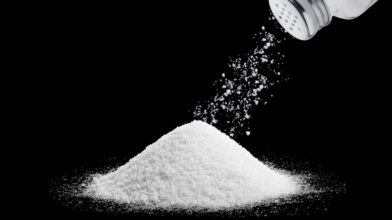 Salt shaker pouring a pile of salt against a black background