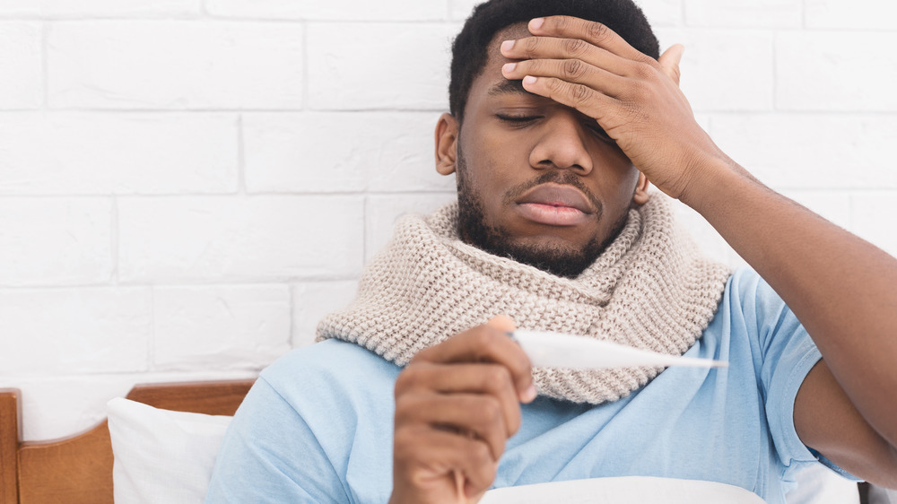 Stock photo of a man feeling ill and checking an oral thermometer