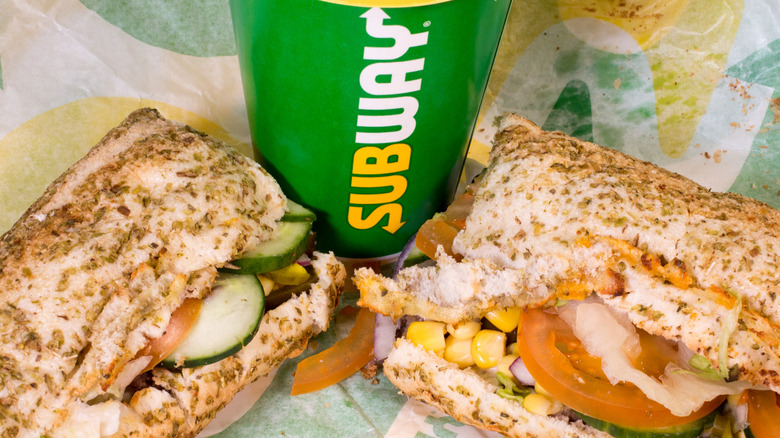 Close up of a Subway soda cup and a footlong sub split in half