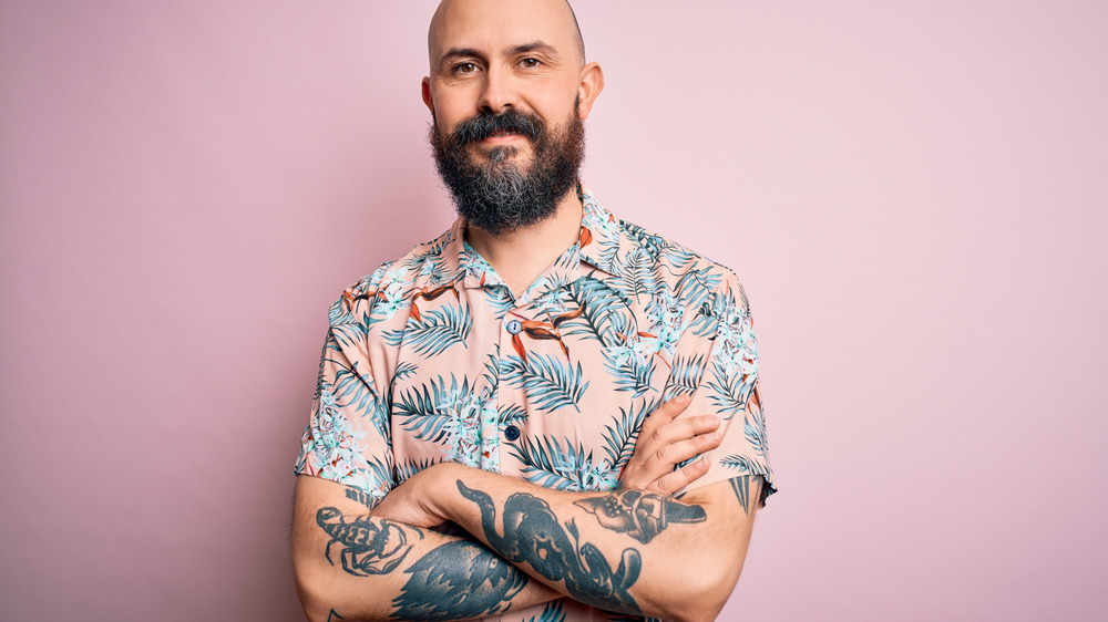 Tattooed man standing in front of pink wall
