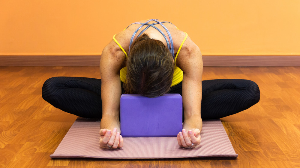 Woman in butterfly stretch resting forehead on yoga block