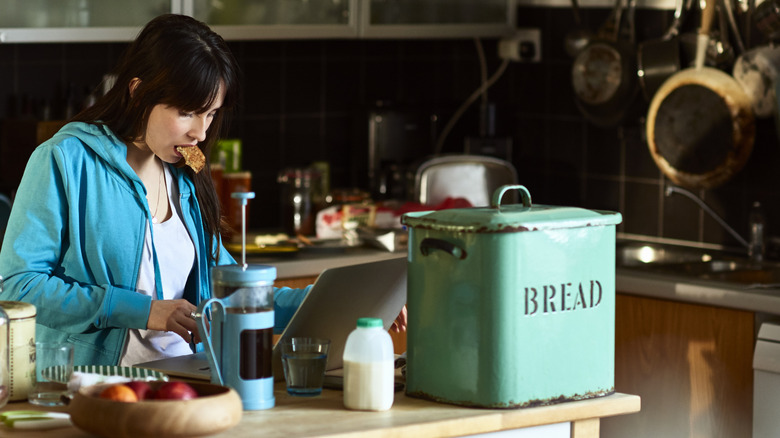 woman eating bread at laptop with bread box in view