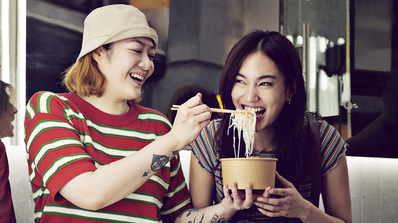 A woman feeding her friend some noodles from a bowl