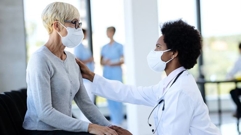 Masked doctor empathetically placing hand on a masked patient's shoulder