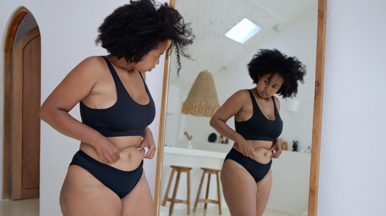 Woman pinching stomach looking at reflection