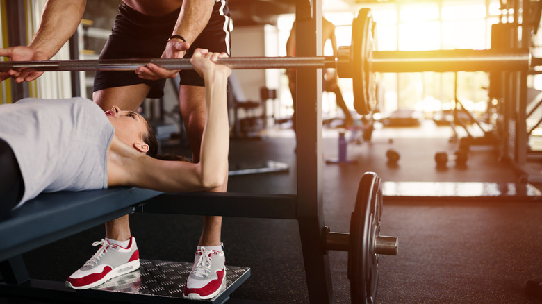 Trainer spotting a woman doing the bench press