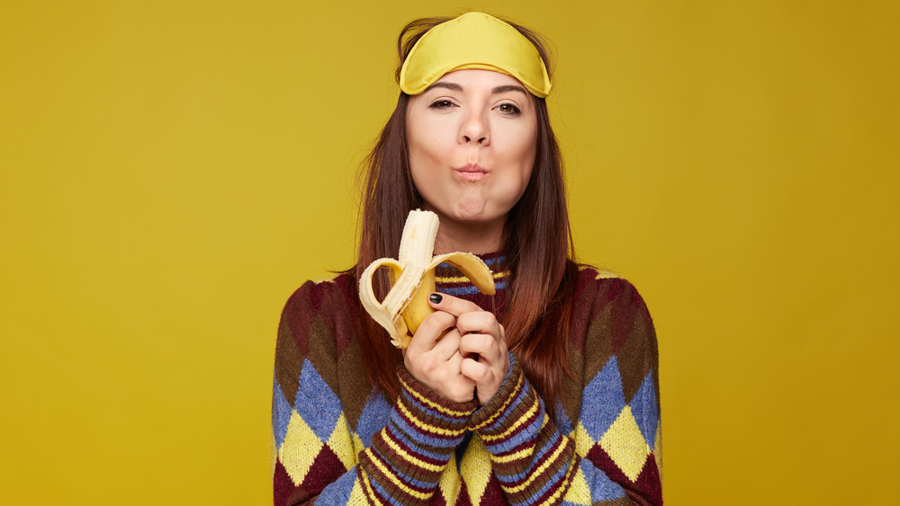Woman in sleep mask eating banana