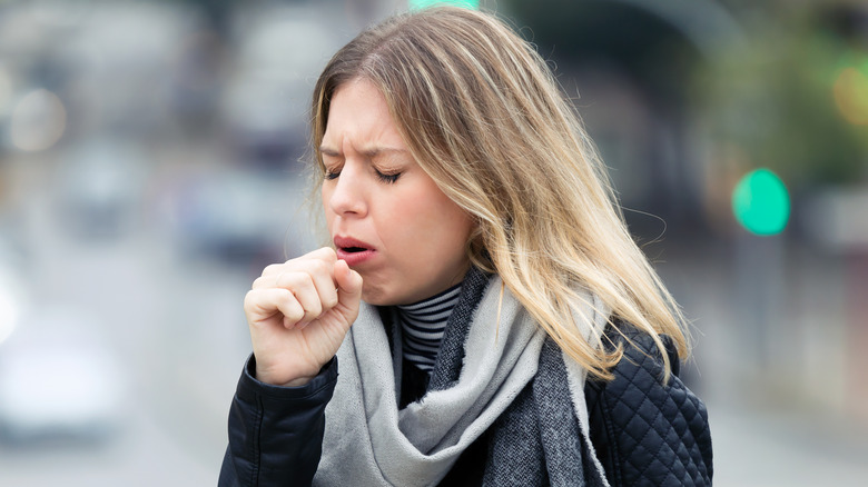 Woman in scarf coughing into her fist