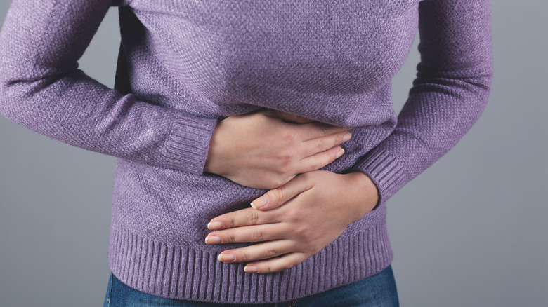 Person in sweater and jeans holding their stomach