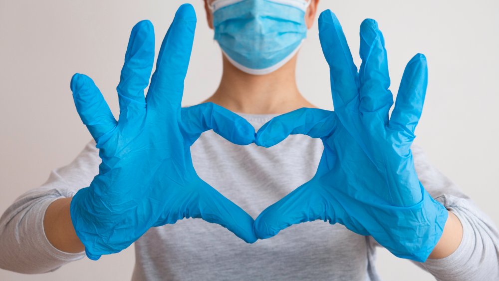 Woman in medical mask and gloves making sign of heart with hands