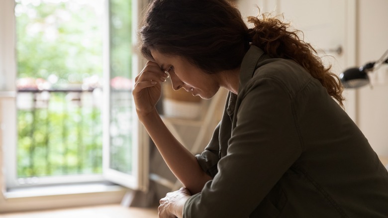 woman sits with hand to forehead