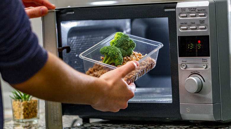 man heating food in plastic container in microwave