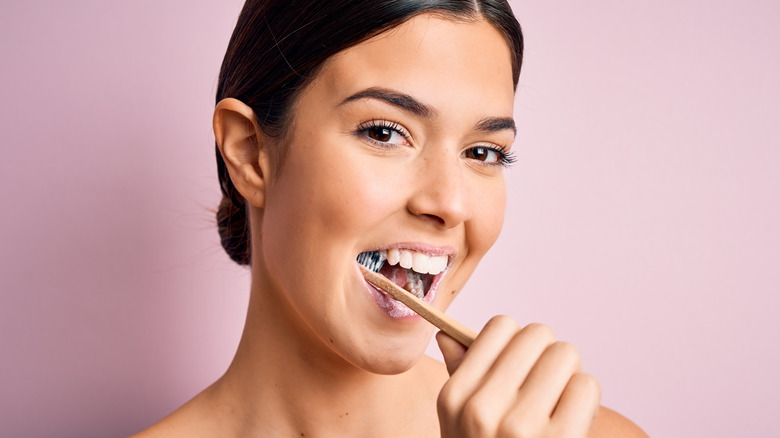 Young woman smiling while brushing her teeth on purple background