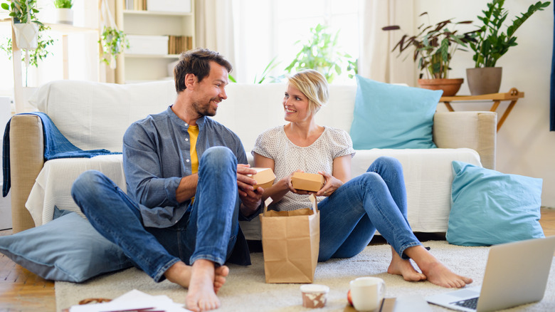 A couple sitting on the floor in their living room eating take-out 