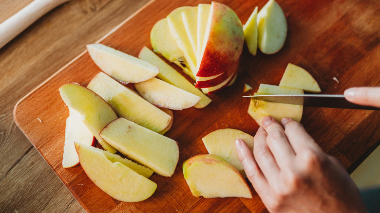 woman's hand slicing apples on a cutting board
