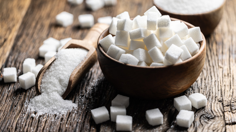 A bowl of sugar cubes next to a scoop of sugar