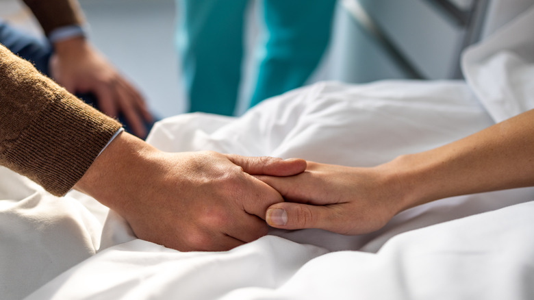 A man is holding the hand of a woman in a hospital bed