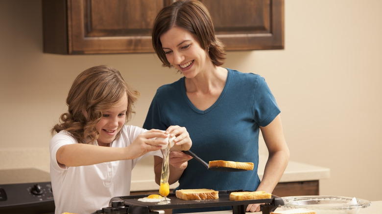 Smiling woman and daughter making eggs