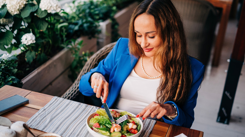 Woman eating a salad topped with shrimp