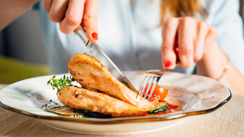 woman cutting into grilled chicken