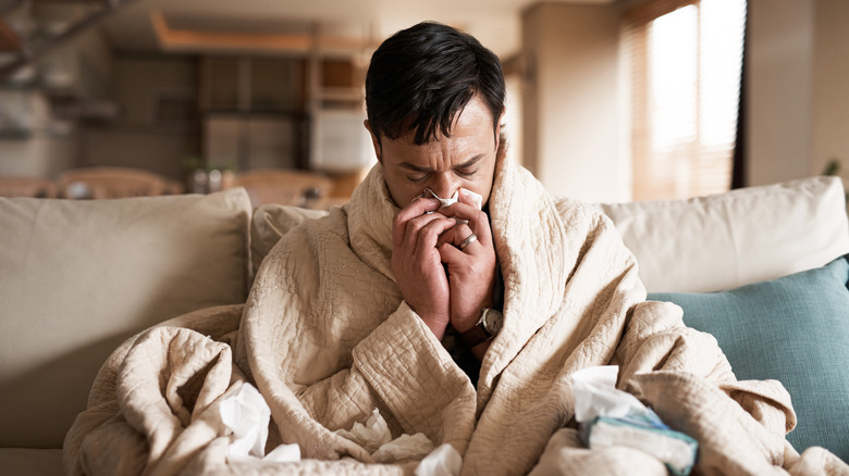 man wrapped in a blanket and blowing his nose
