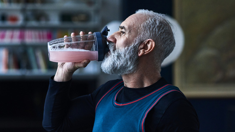 A mature man drinking a pink beverage