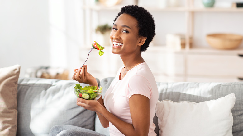 Woman smiling on the couch eating a salad