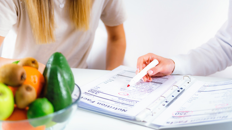 Woman coaching another woman on nutrition facts at a desk with fruit