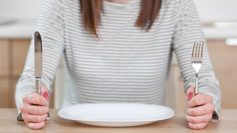 young woman holding a fork and knife over an empty plate 