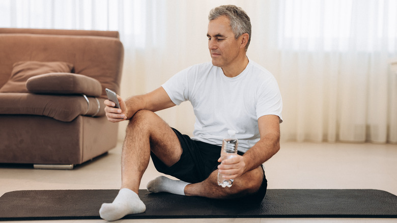 man texting while sitting on a yoga mat 