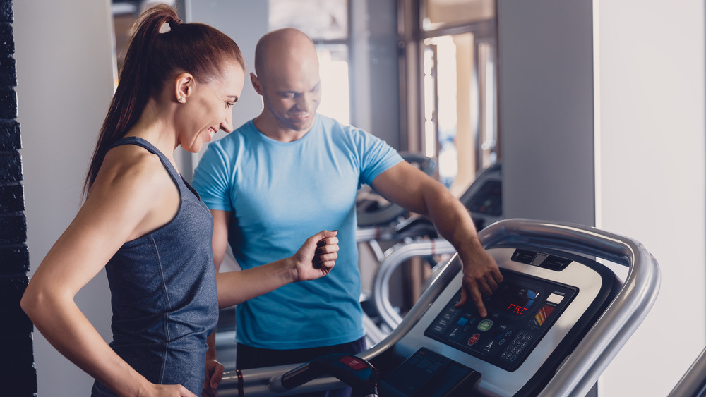 Woman on a treadmill getting help from a personal trainer