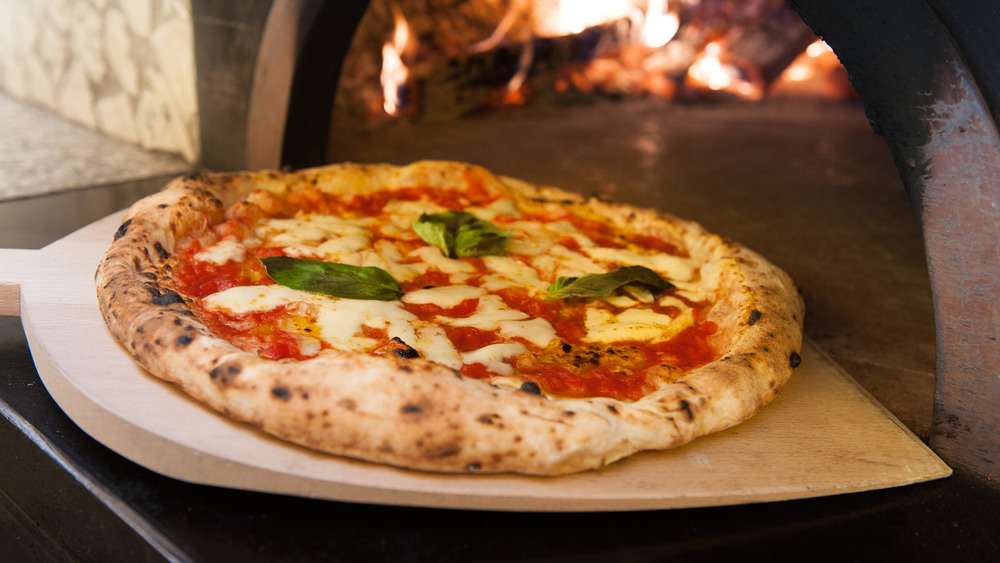 A Neapolitan pizza on a pizza paddle in front of an open brick oven