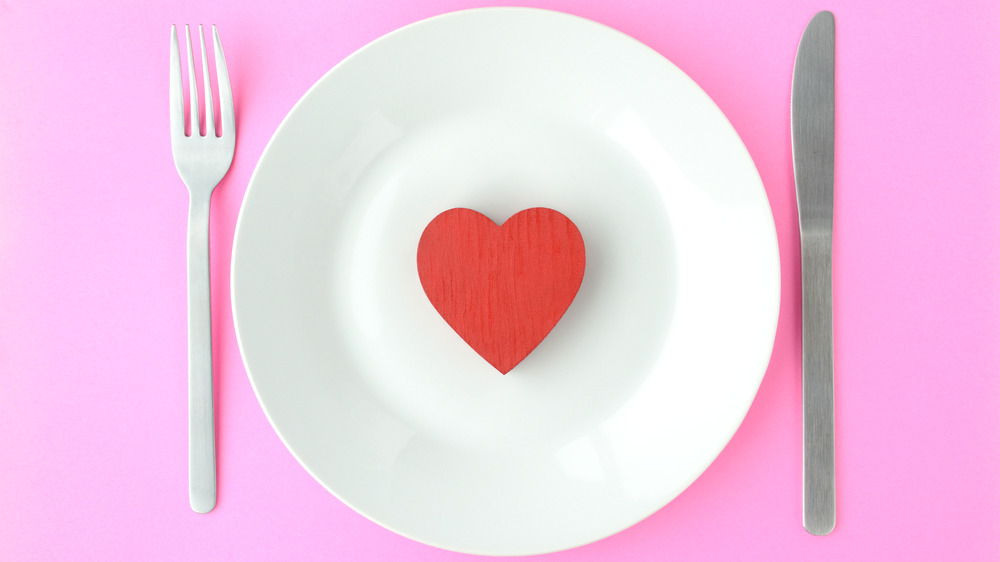 heart on a plate with fork and knife. Pink background