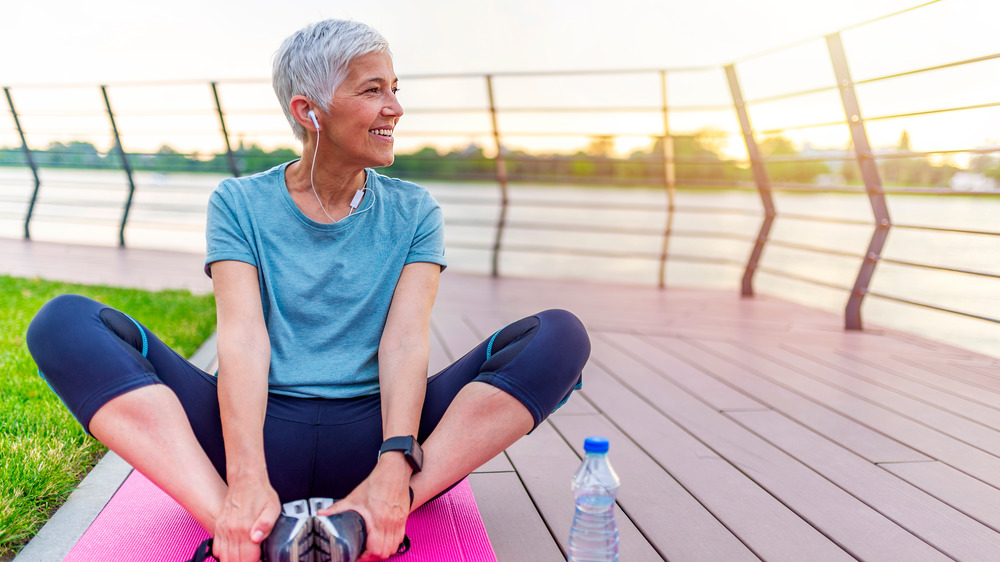 An older women stretching outside on a pink yoga mat 