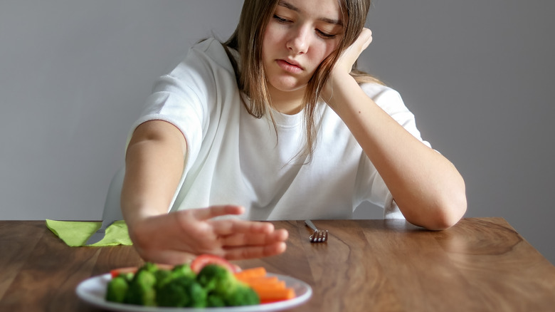 teenager pushing plate with vegetables