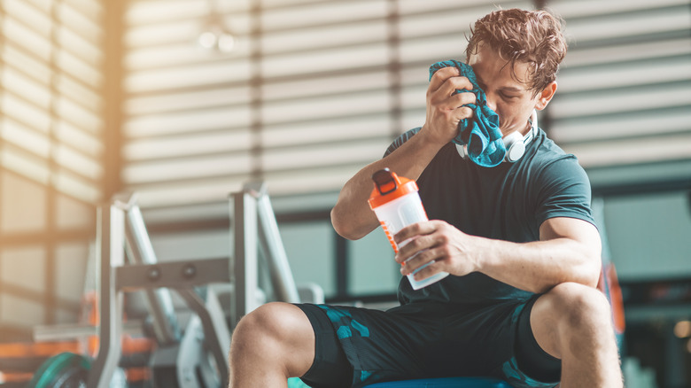 A man drinks pre-workout on a bench at the gym
