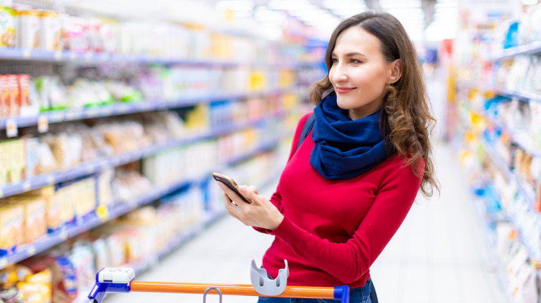 A woman grocery shopping with her phone