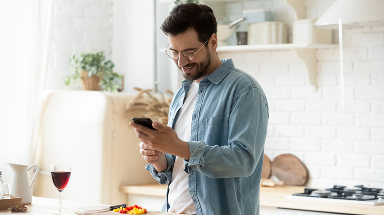 A man cooking food while looking at his phone