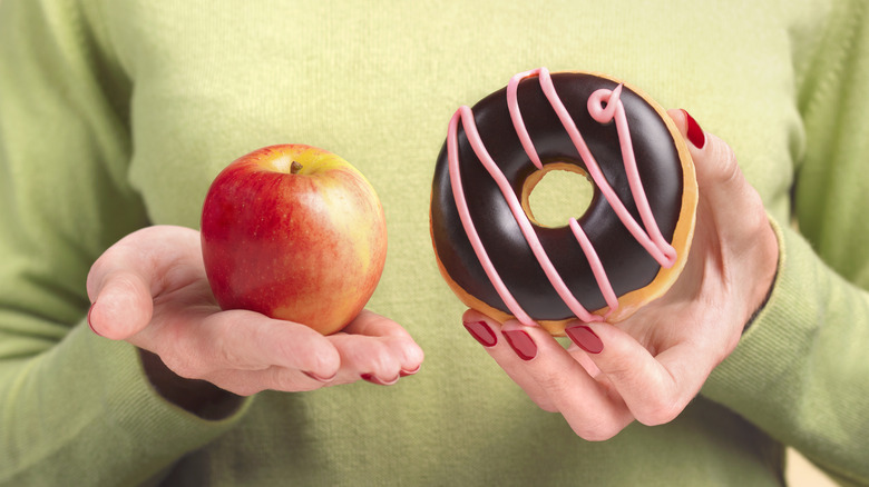 woman's hands holding apple and doughnut