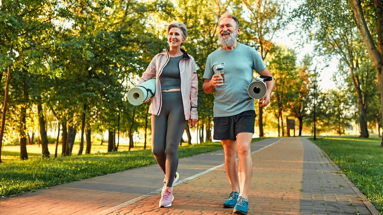 middle age couple walking on path carrying yoga mats